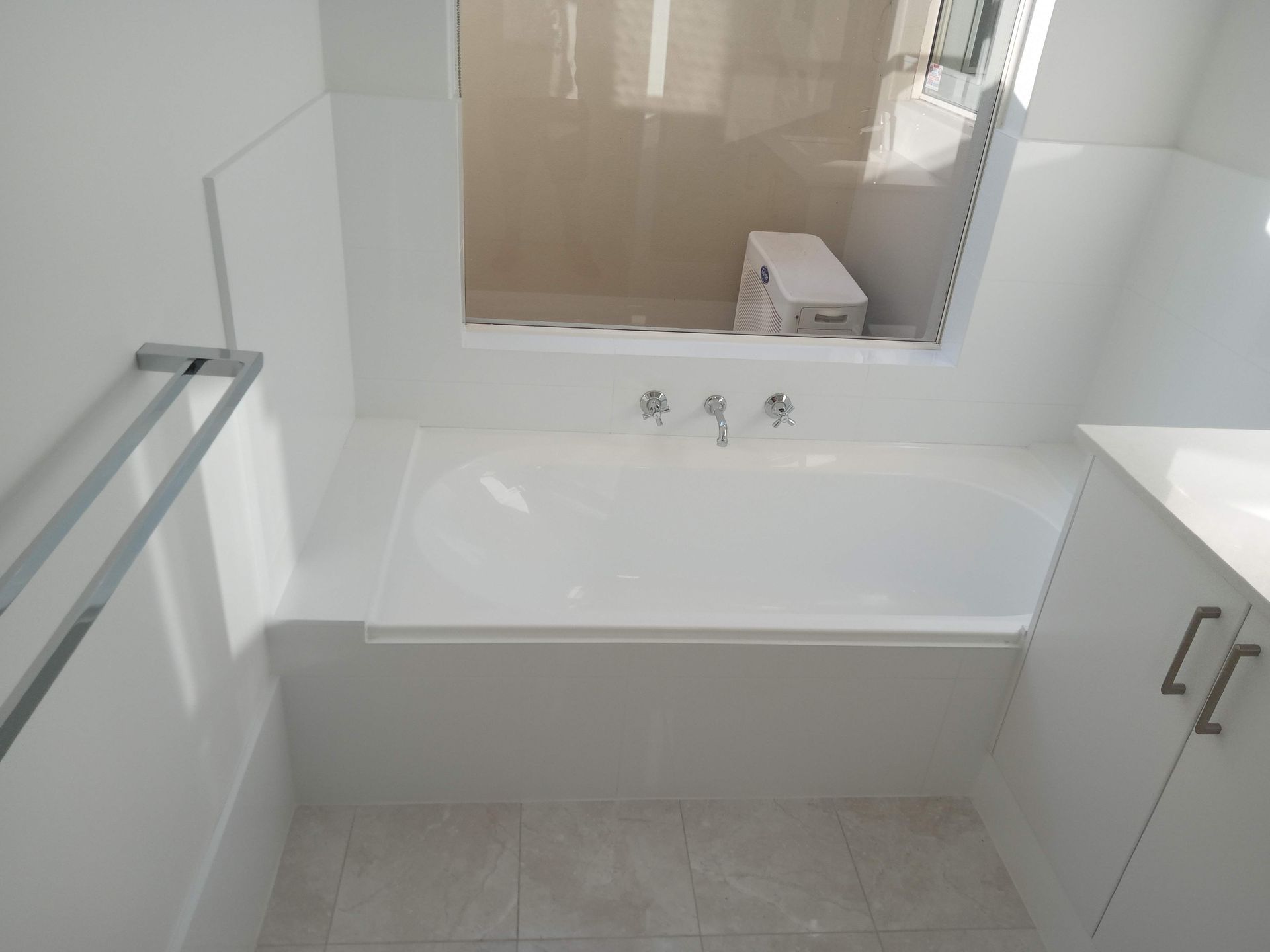White bathtub built into a wall, chrome faucet, and towel rack in a bathroom.