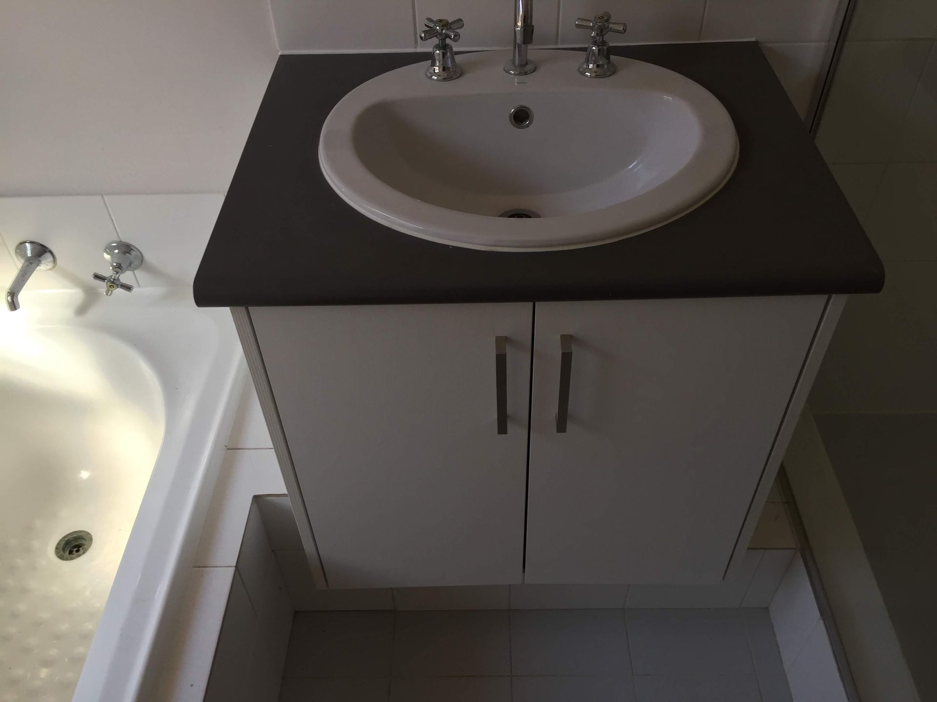 Bathroom vanity with oval sink, dark gray countertop, white cabinet, and silver faucet.