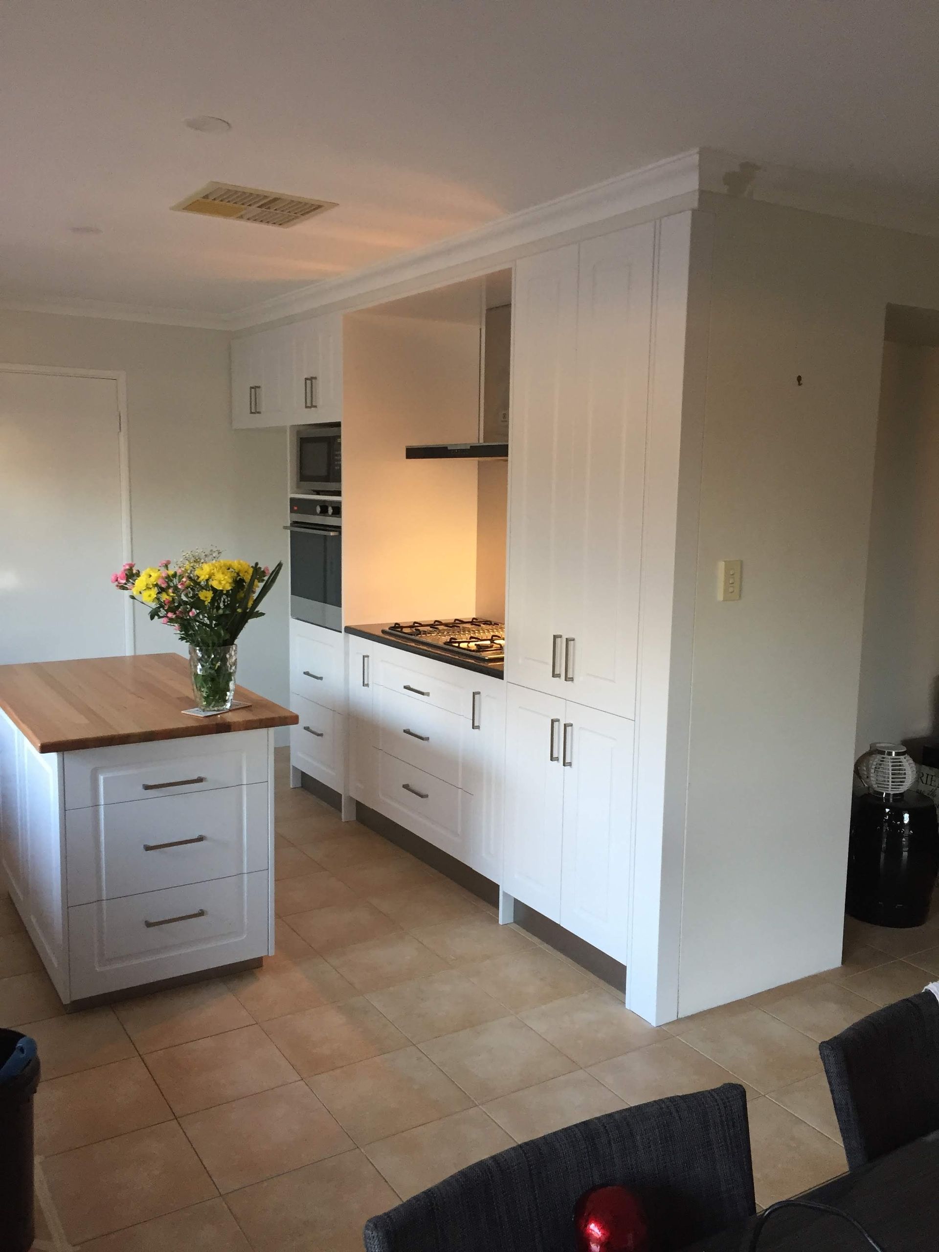 White kitchen with island, appliances, cabinets, and beige tiled floor.