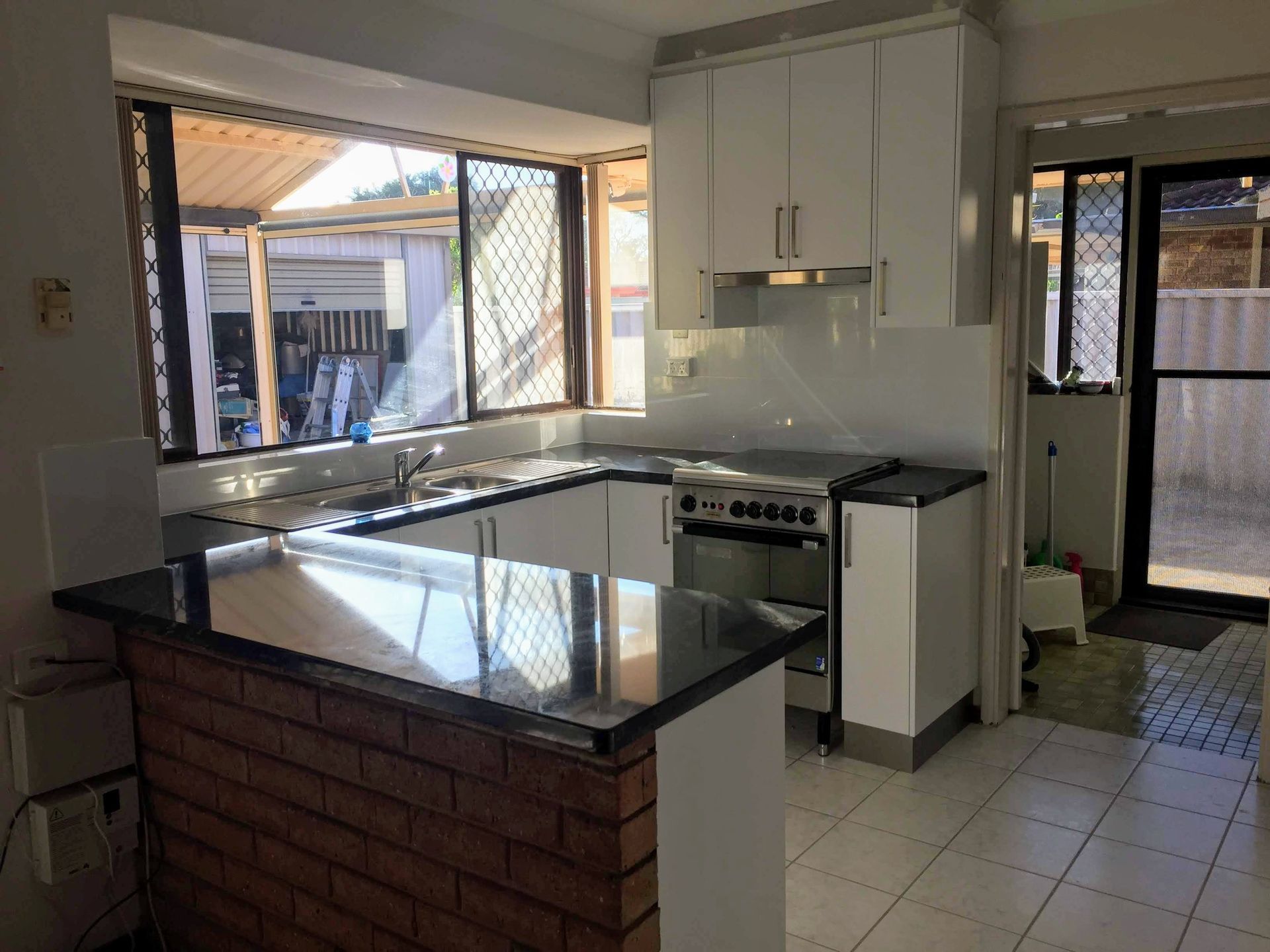 Kitchen with white cabinets, black countertops, brick island, and a large window.