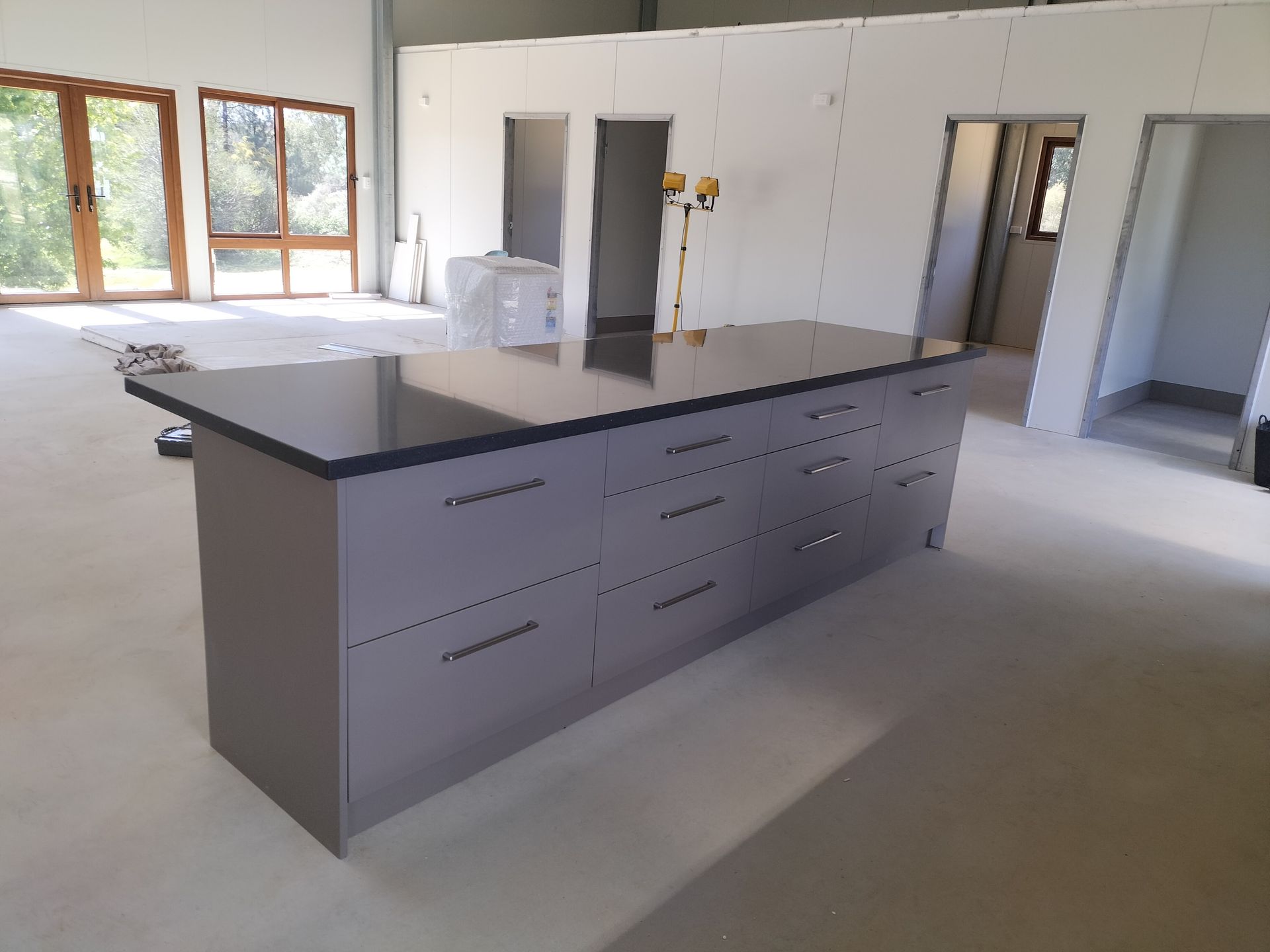 Gray kitchen island with dark countertop in a room under construction.