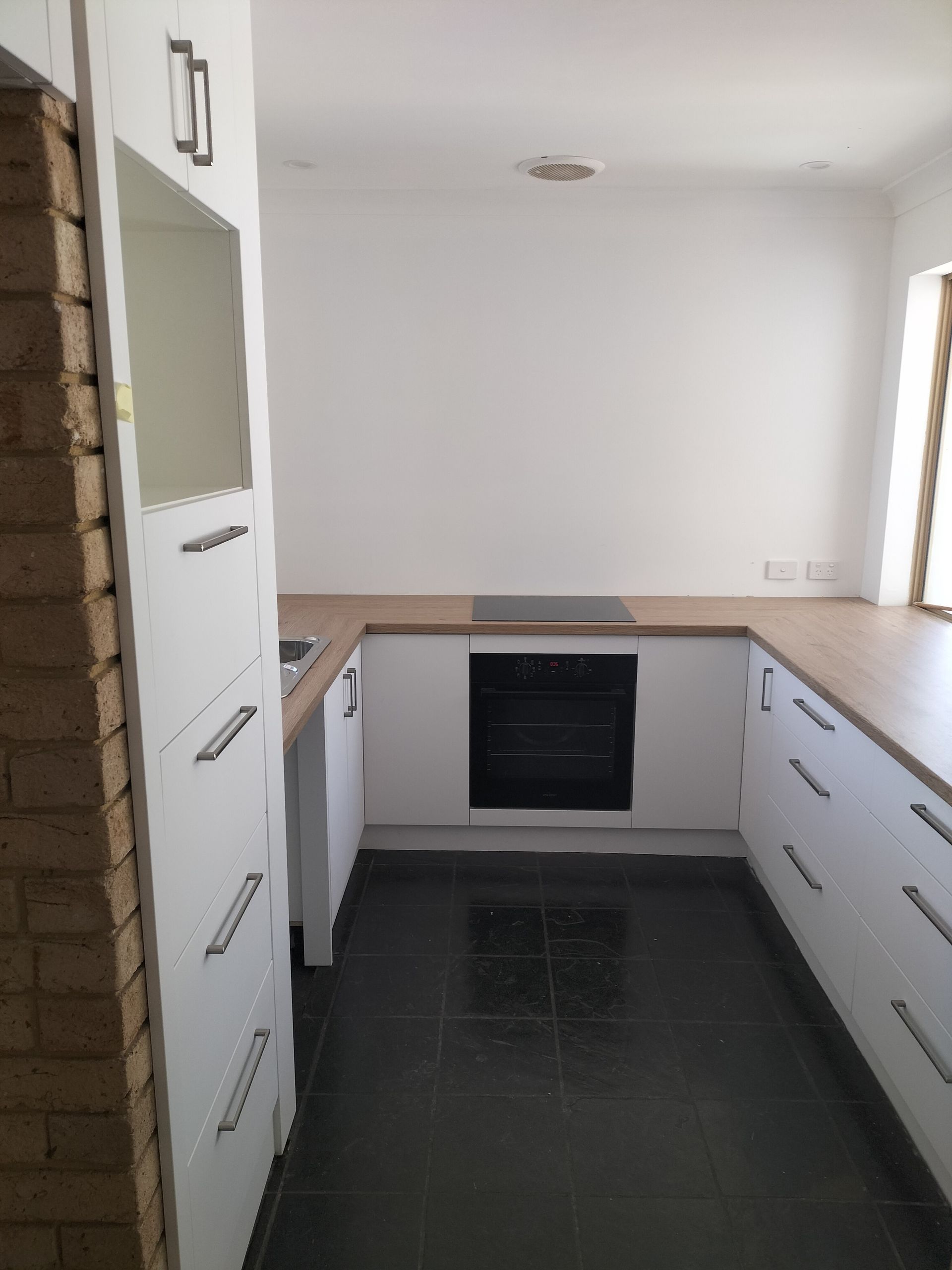 White kitchen with wood countertops, black tile floor, and a brick wall.