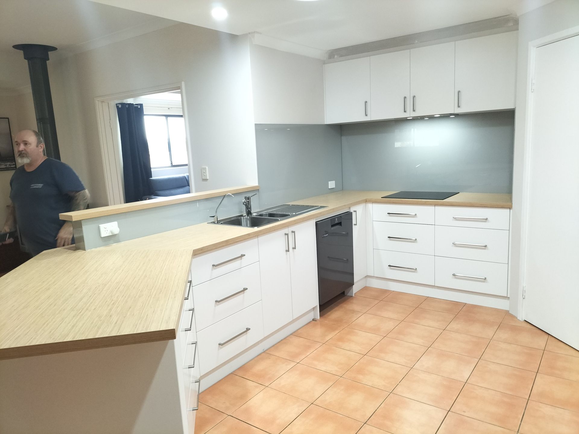Kitchen with white cabinets, wooden countertops, and a person standing.