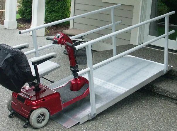 Red mobility scooter on a metal ramp with railings, providing accessibility to a building.