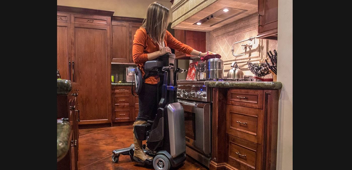 A woman in a wheelchair is standing in a kitchen next to a stove.