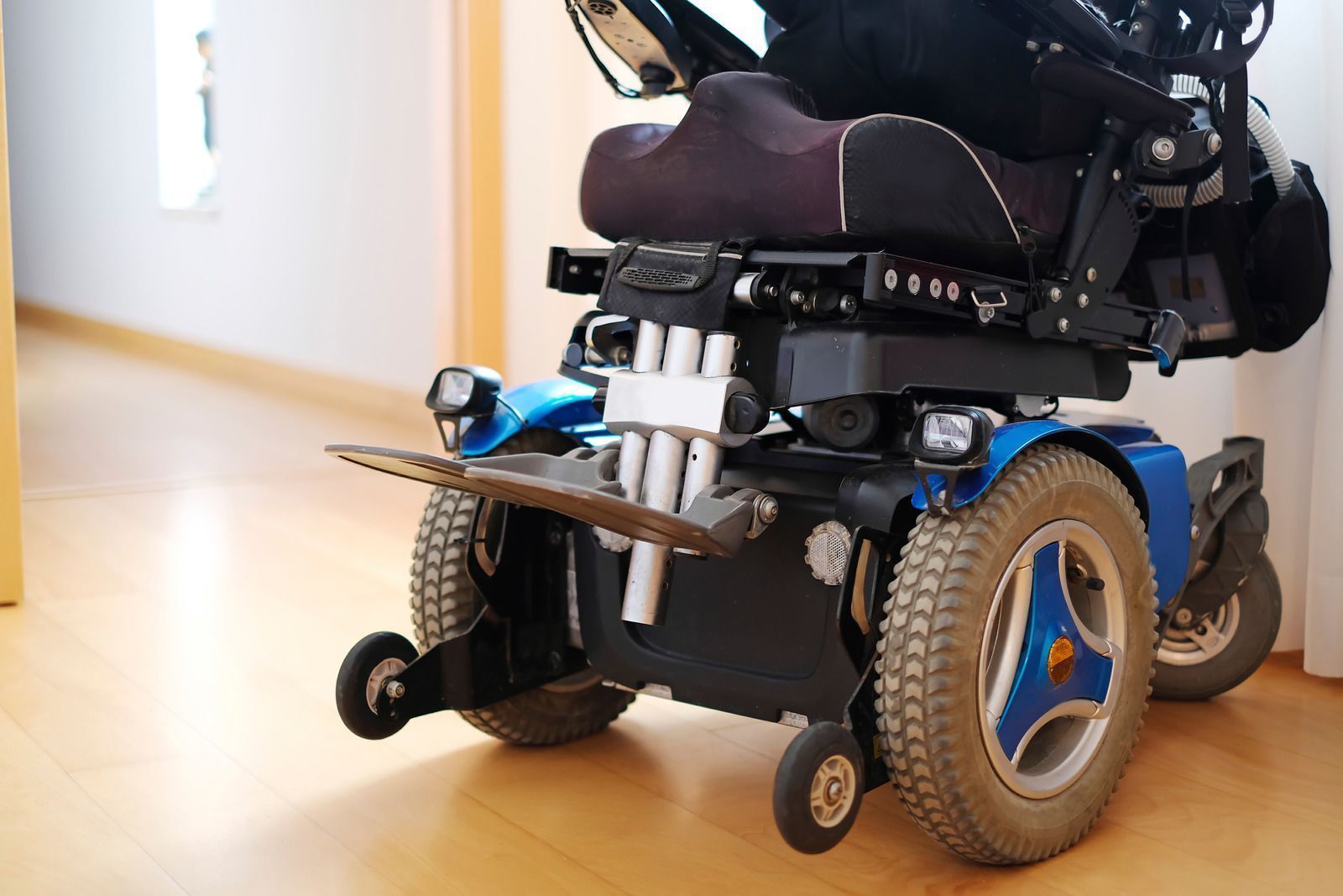 Blue and black power wheelchair in a room with light wood flooring, angled towards the viewer.