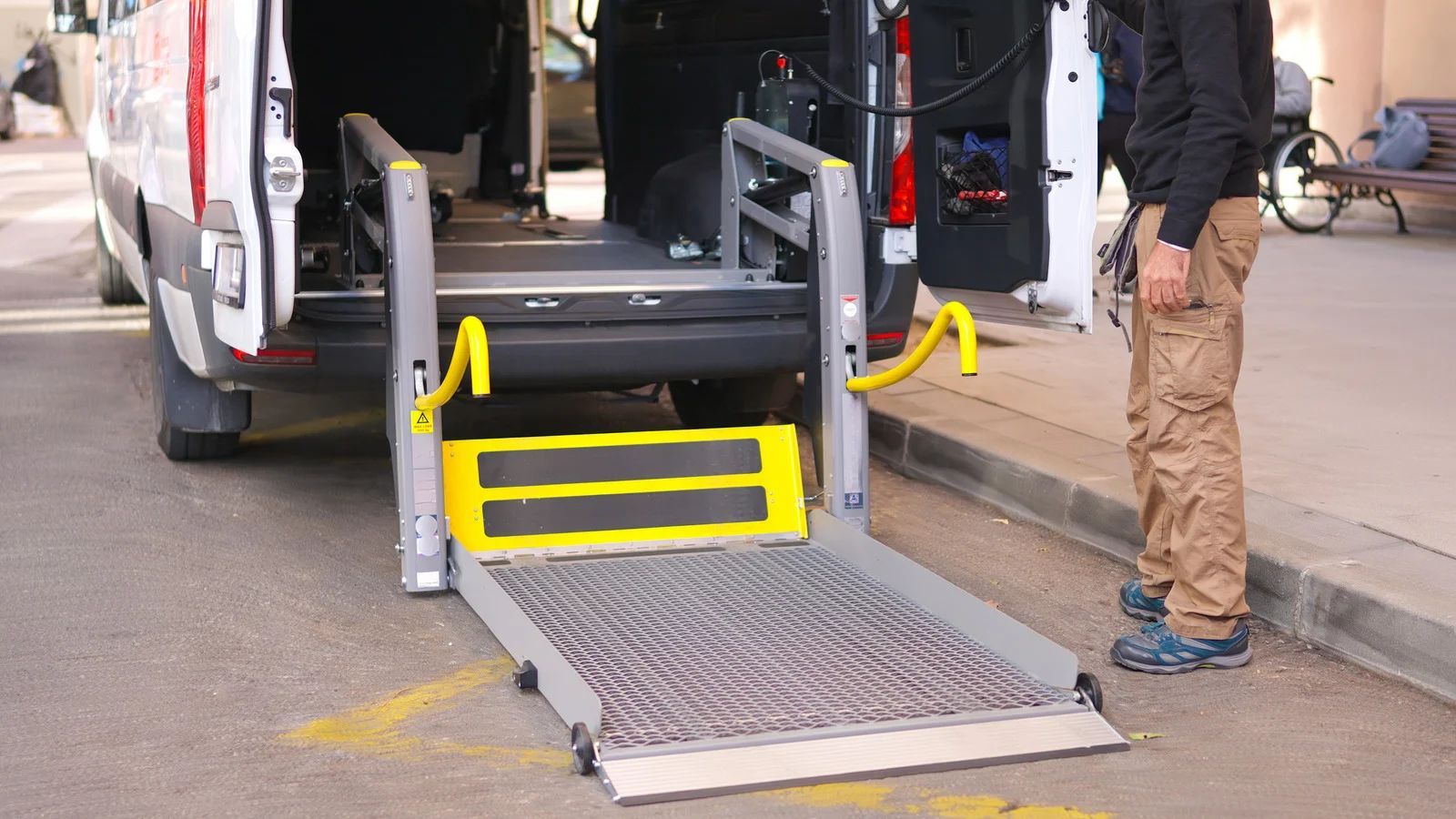 A wheelchair lift is deployed from the back of a van onto the ground, with a person standing nearby.