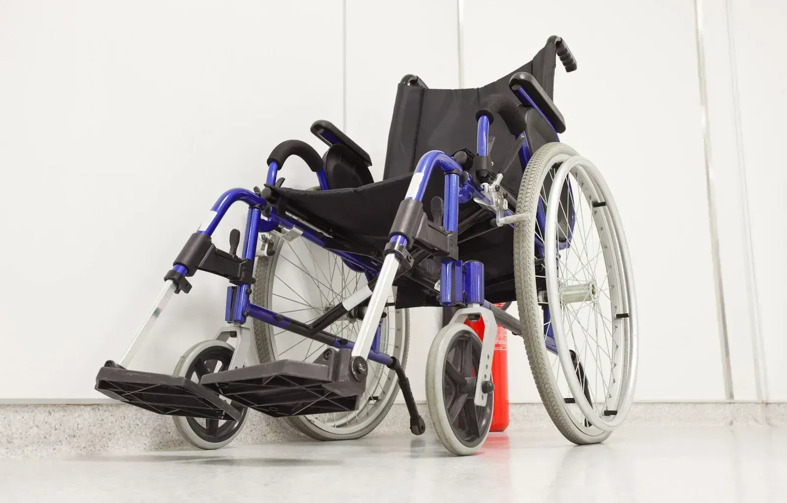 A blue and black wheelchair is leaning against a wall.