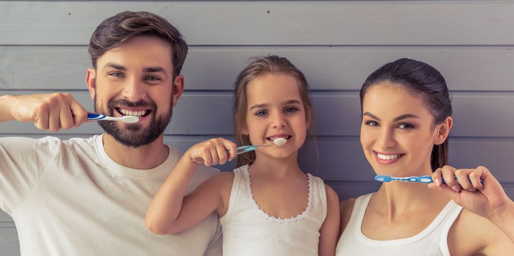 A man , woman and child are brushing their teeth together.