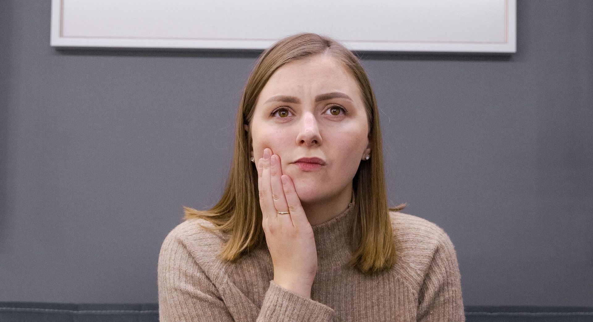 A woman is sitting on a couch with her hand on her face.