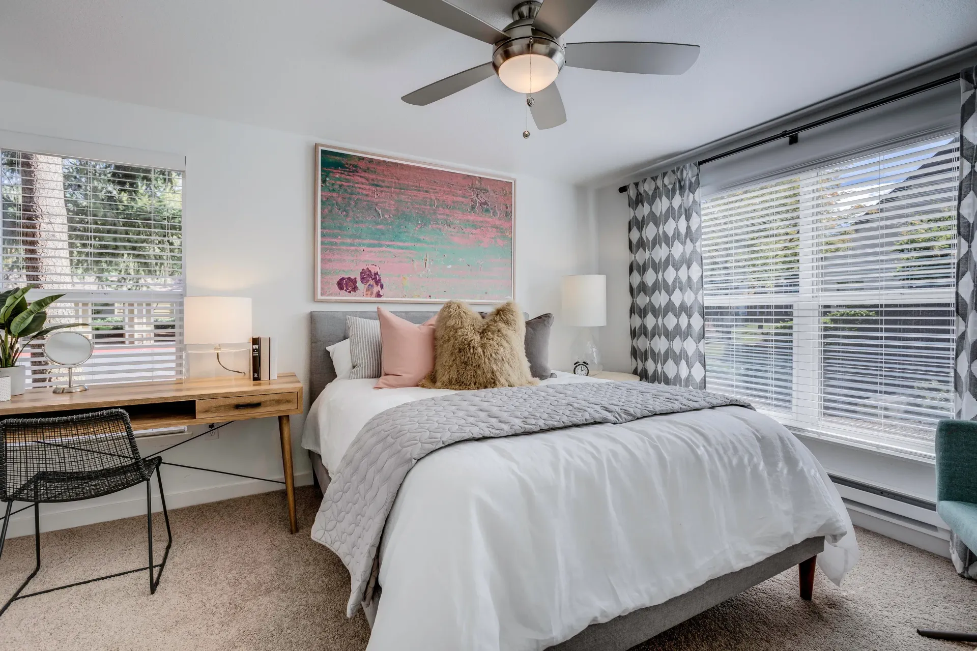 Bright bedroom in a modern apartment with a bed, desk, and large windows.