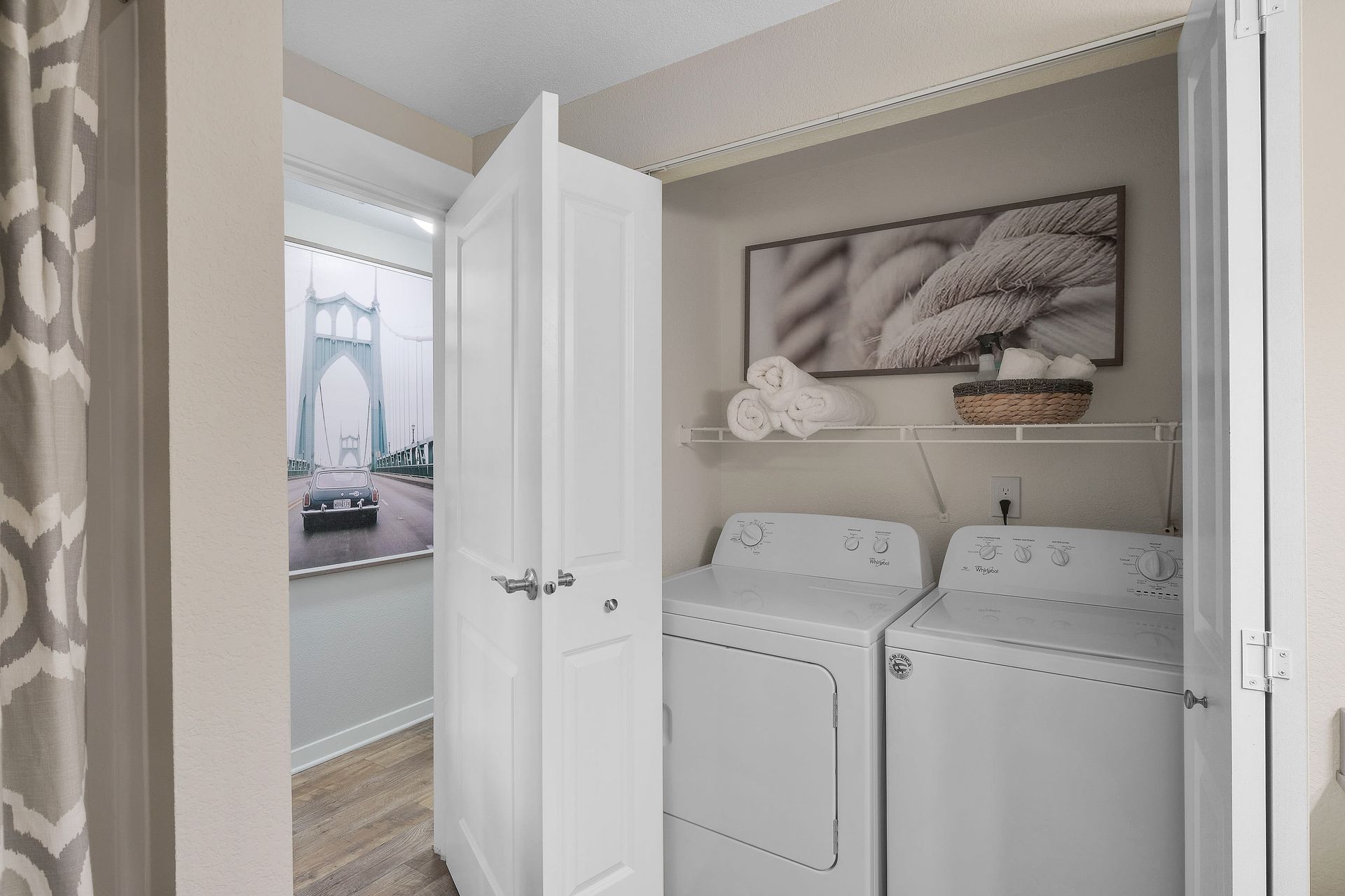 In-unit laundry closet with a washer and dryer, shelf with towels, and rope-art wall decor.