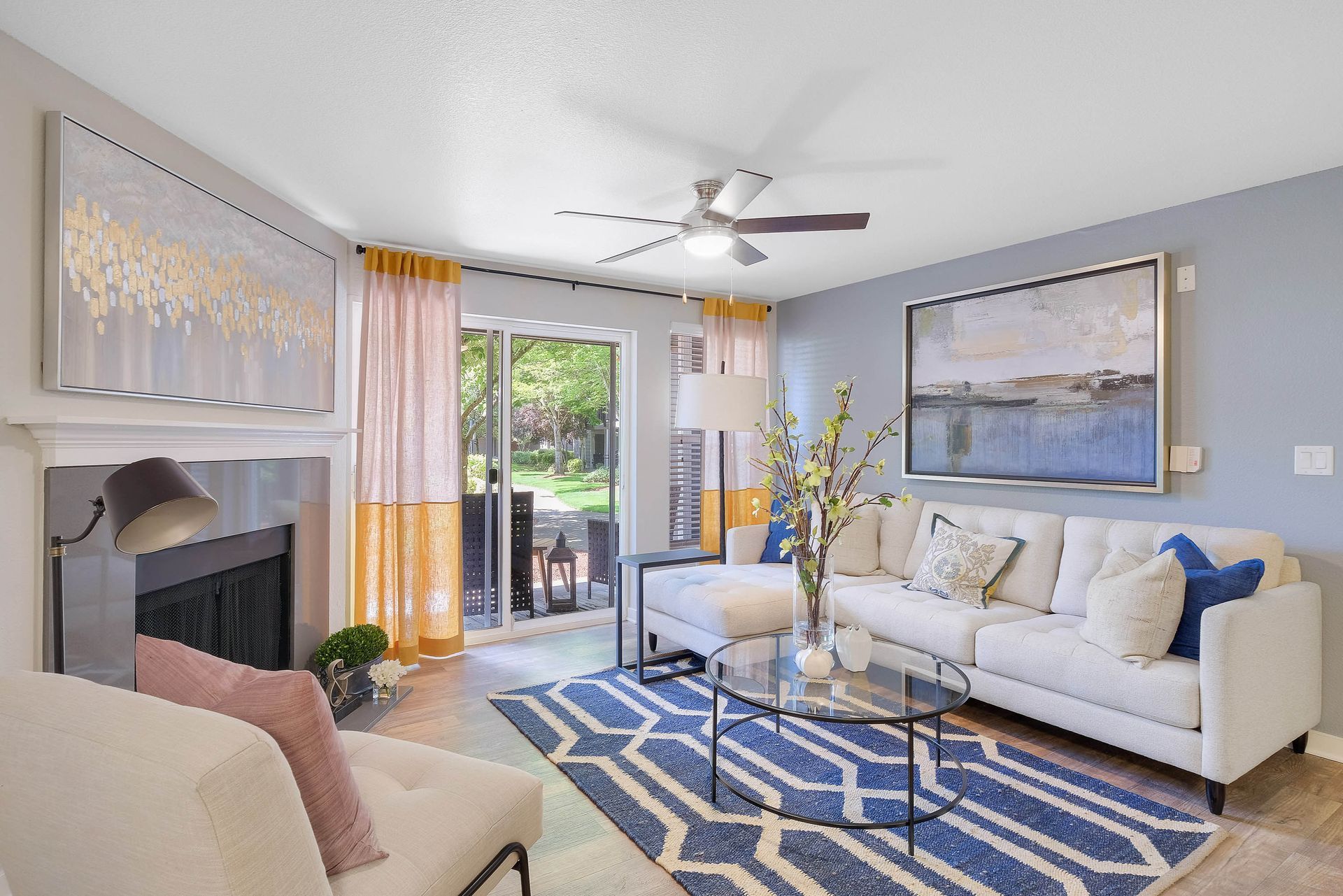 Bright living room in an apartment with a beige sofa, glass coffee table, fireplace, and sliding glass doors to the patio.