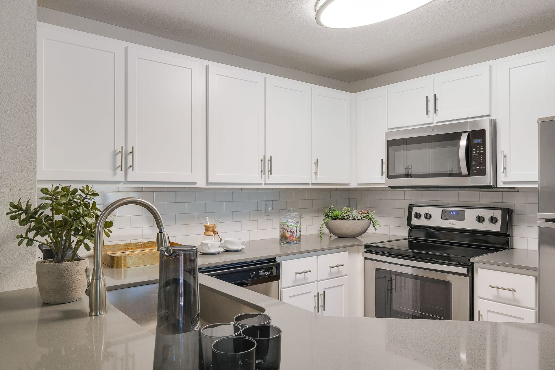 Modern white kitchen with stainless steel appliances and gray countertops.