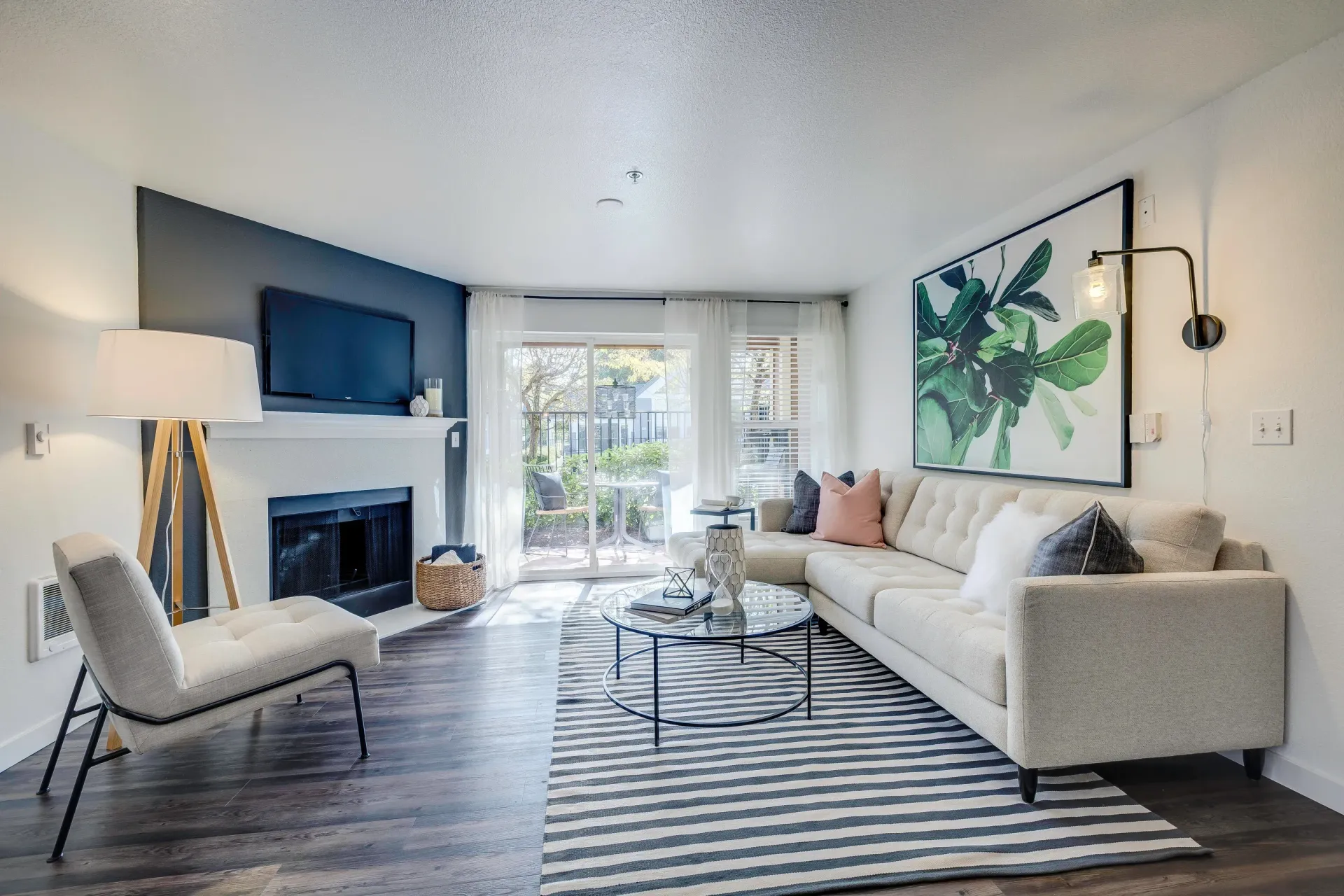 Living room in a modern apartment with a beige sectional, fireplace, TV mounted above mantel, and glass sliding door.