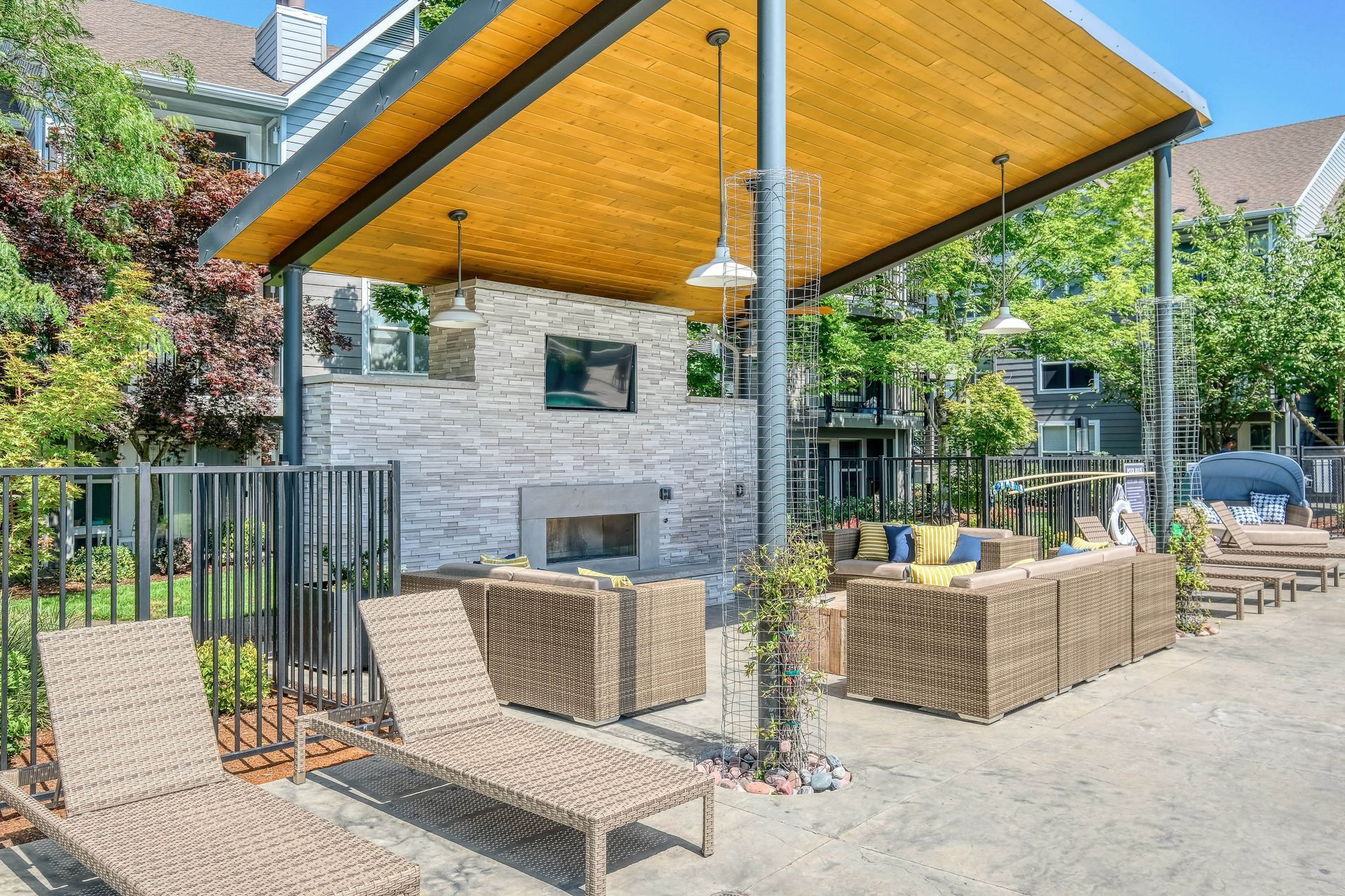 Outdoor community lounge with wicker seating under a wood canopy and a wall-mounted TV.