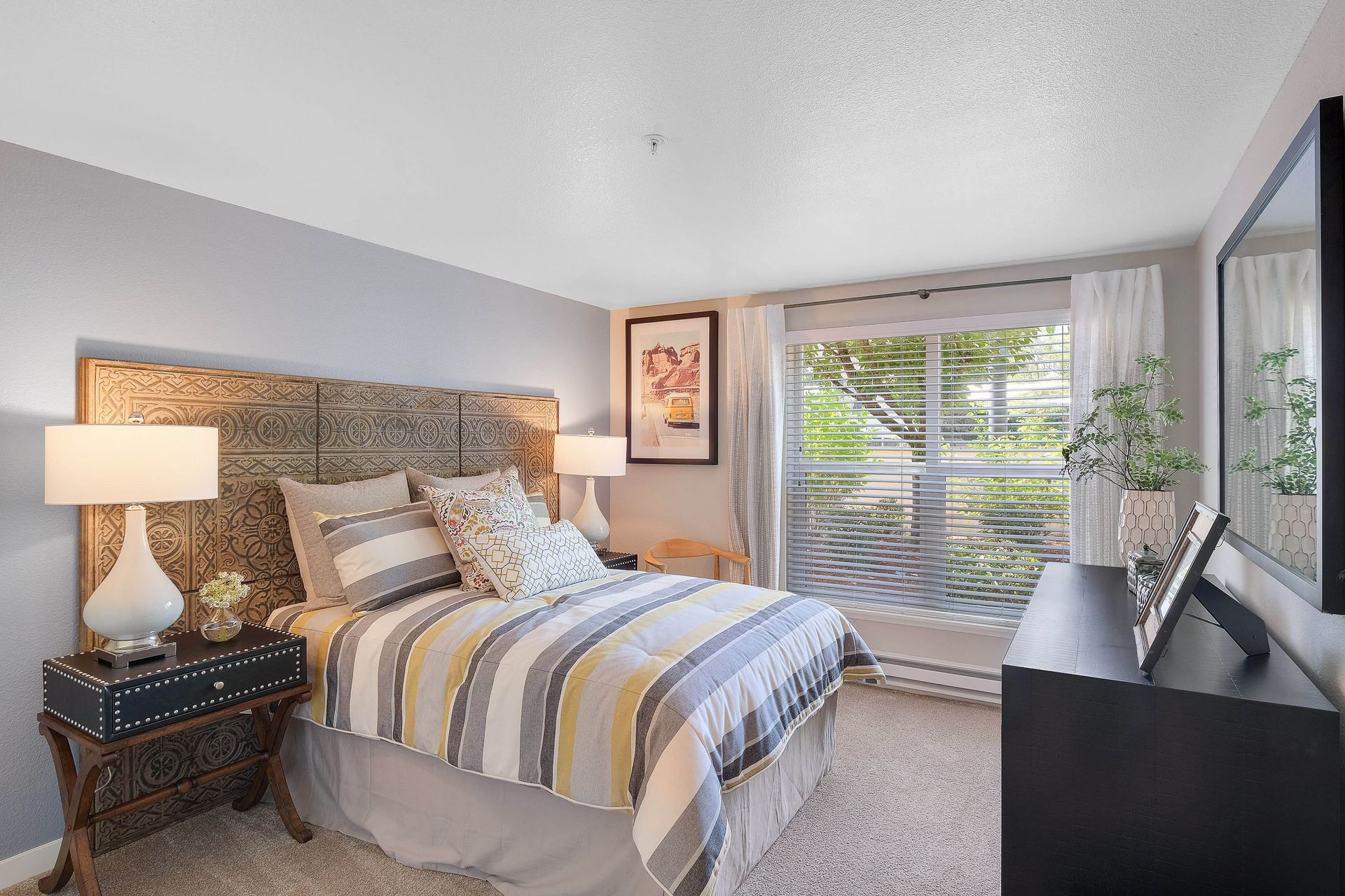 Bedroom with a patterned headboard, striped bedding, two nightstands, and a large window.