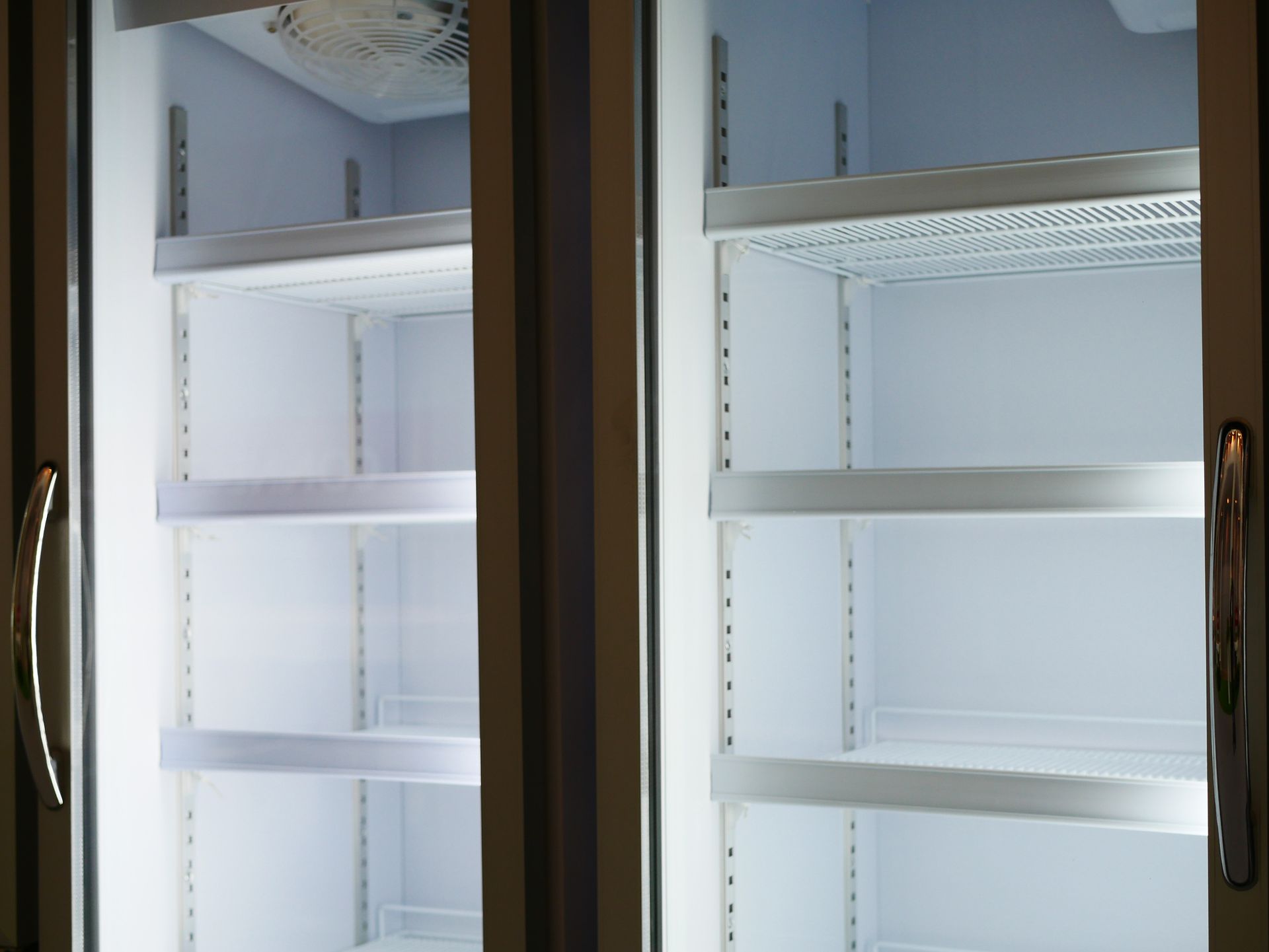 Two empty refrigerators with glass doors and shelves