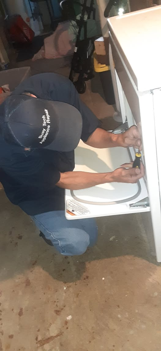 A man is fixing a washing machine with a screwdriver.