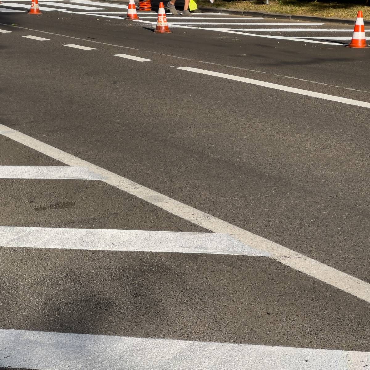 Asphalt road with white painted lines, orange traffic cones, and a crosswalk.