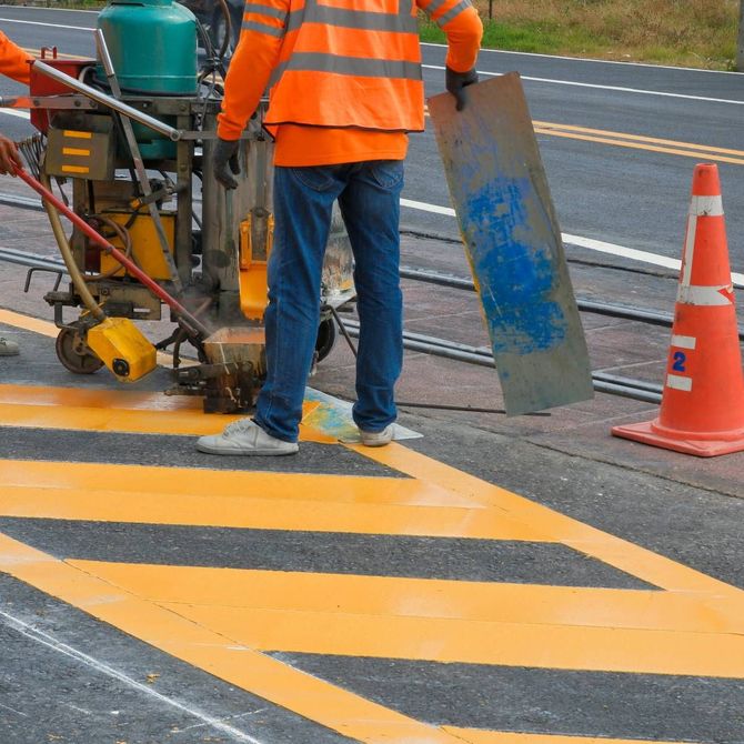 Close-up of fresh asphalt being laid, with a yellow and red steamroller in the background.