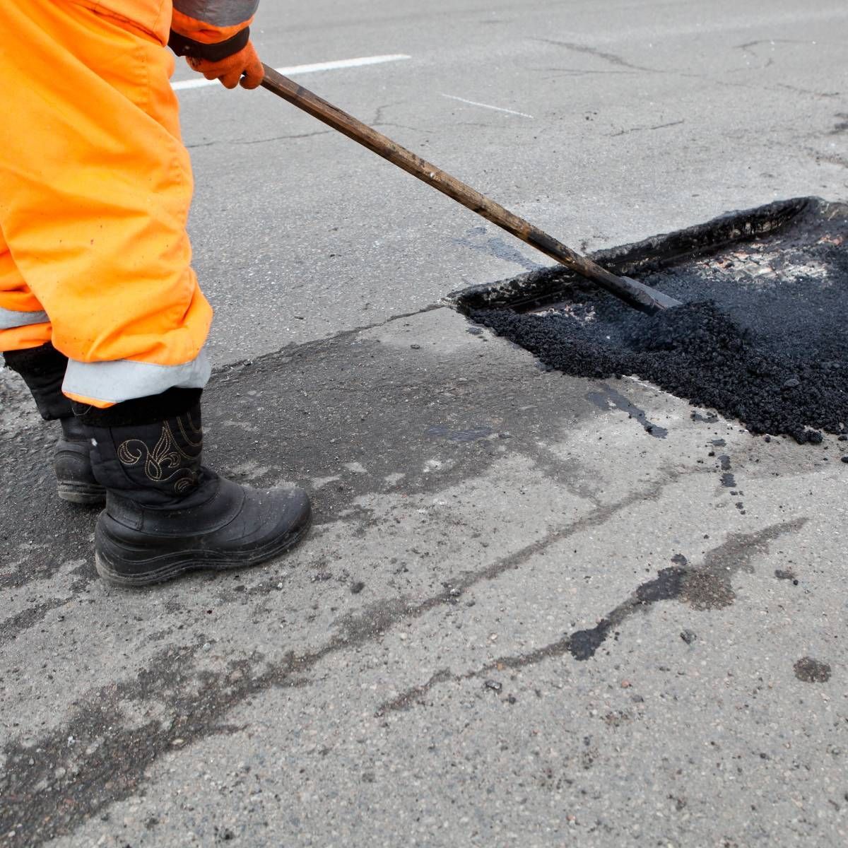Person in orange workwear patching asphalt on a road.