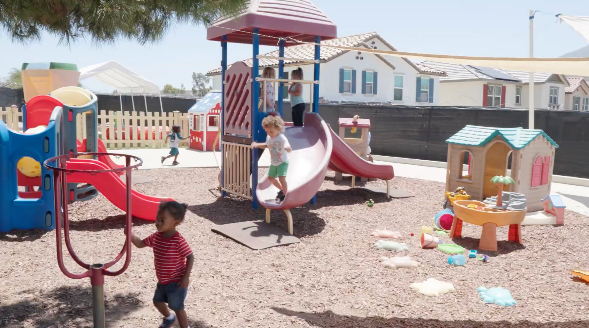 Children playing on colorful playground equipment in a sandy outdoor park on a sunny day