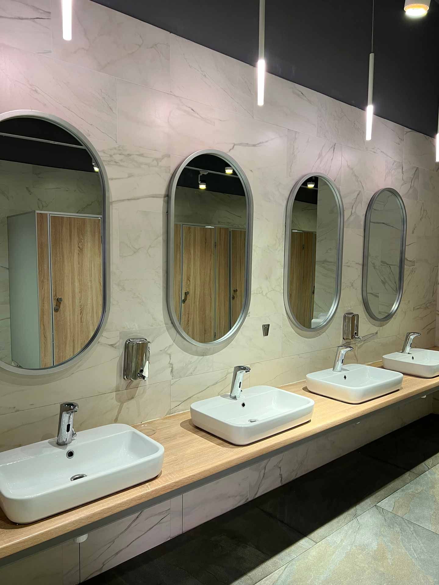 Public restroom with white sinks, oval mirrors, and wood stalls.