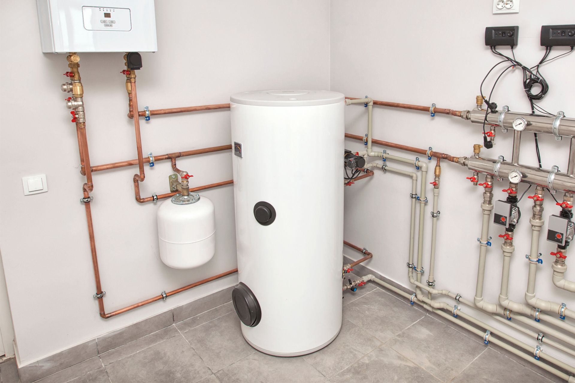 White water heater and related plumbing in a utility room. Copper and white pipes against gray walls.