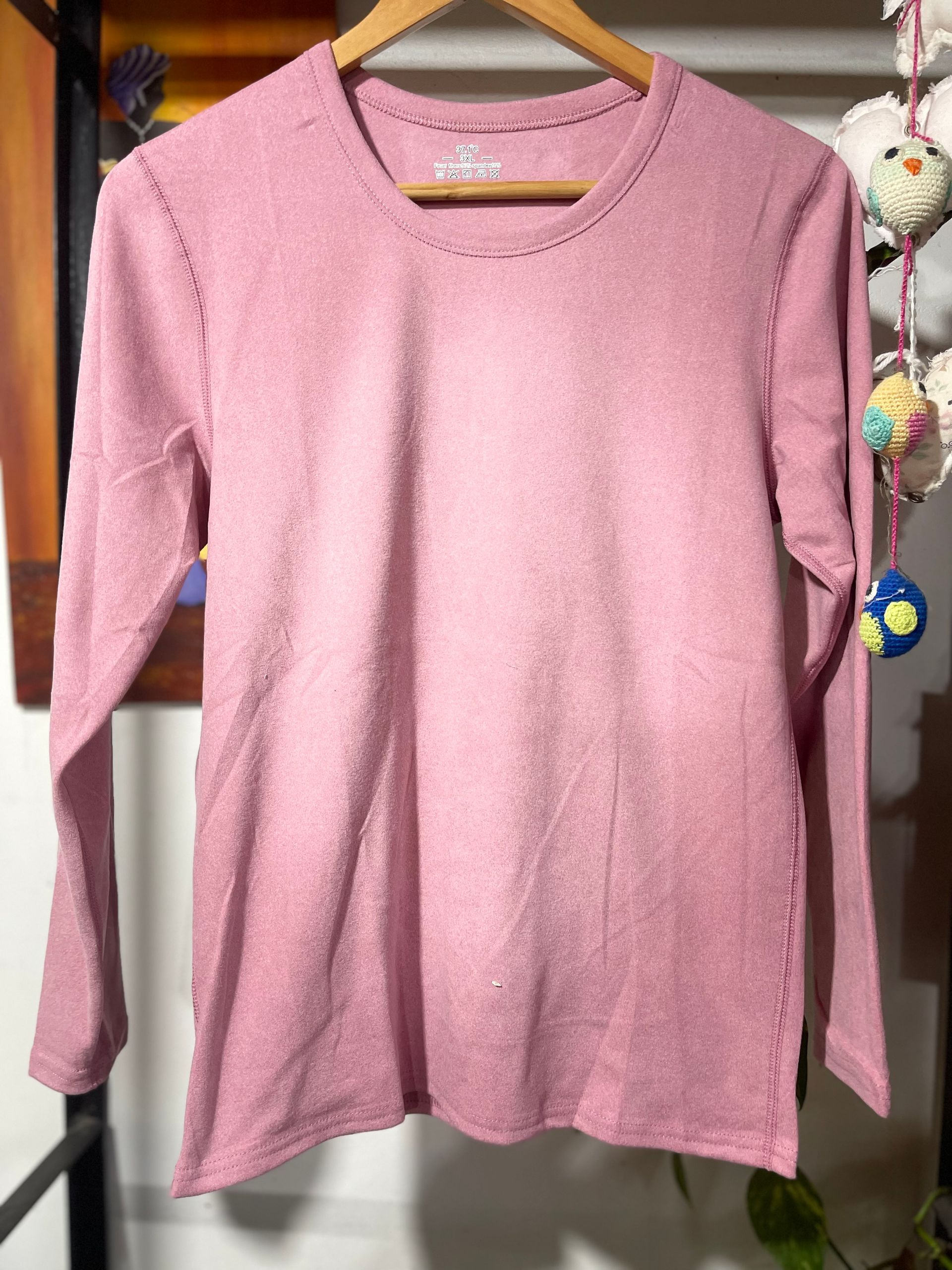 Una camisa rosa con mangas largas está colgada en una percha.