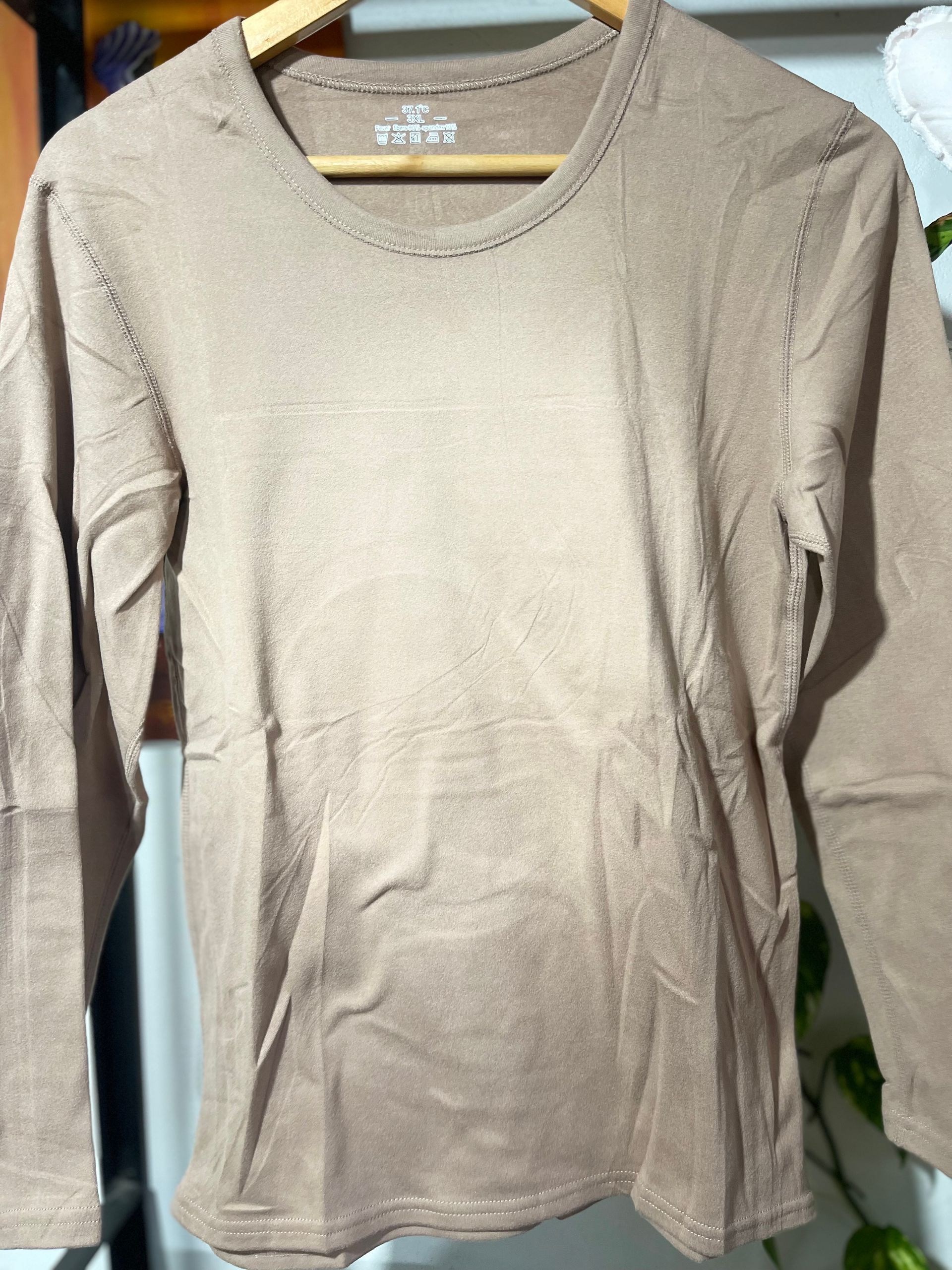 Una camisa marrón con mangas largas cuelga de una percha de madera.