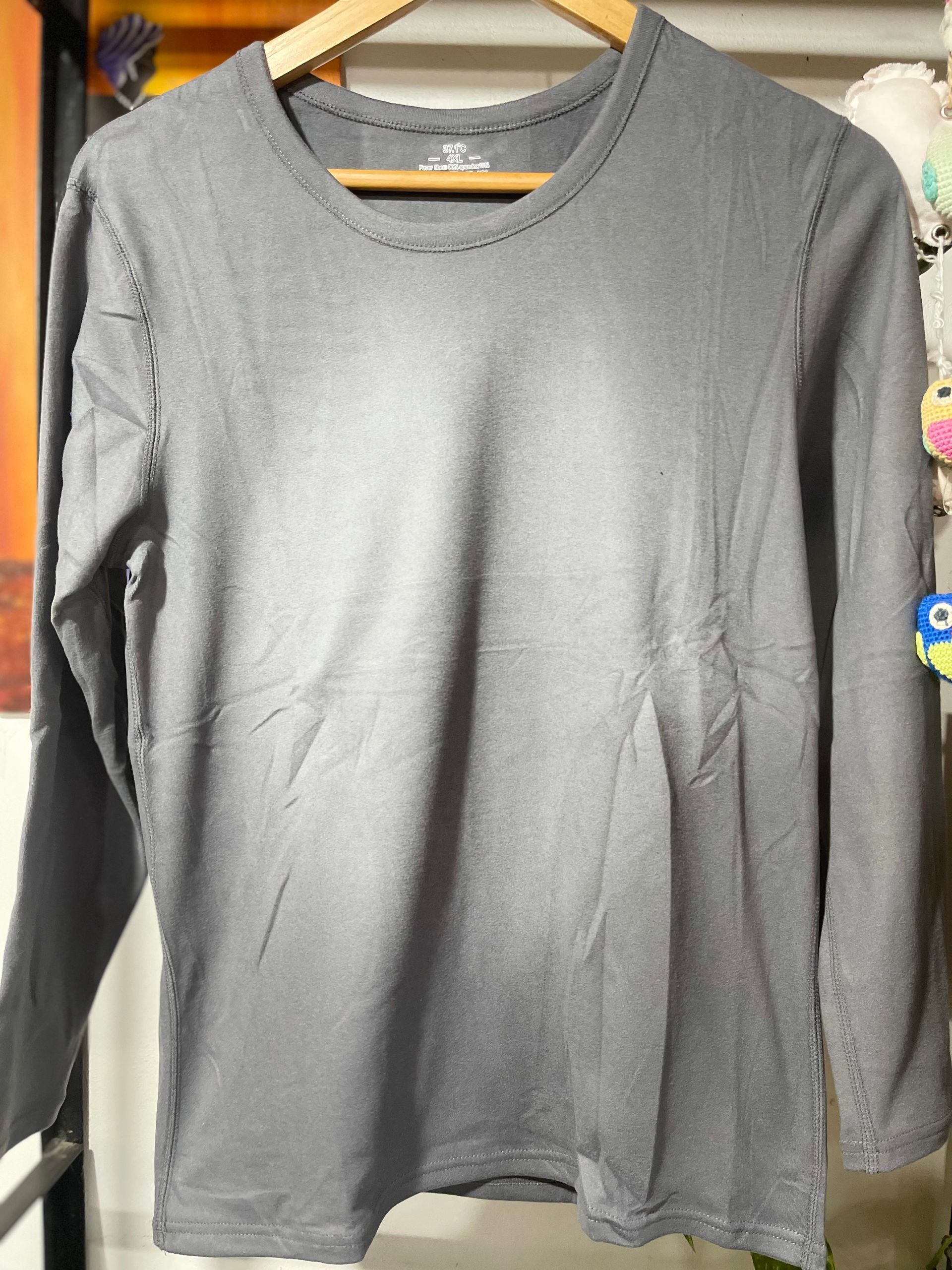 Una camisa gris con mangas largas está colgada en una percha de madera.