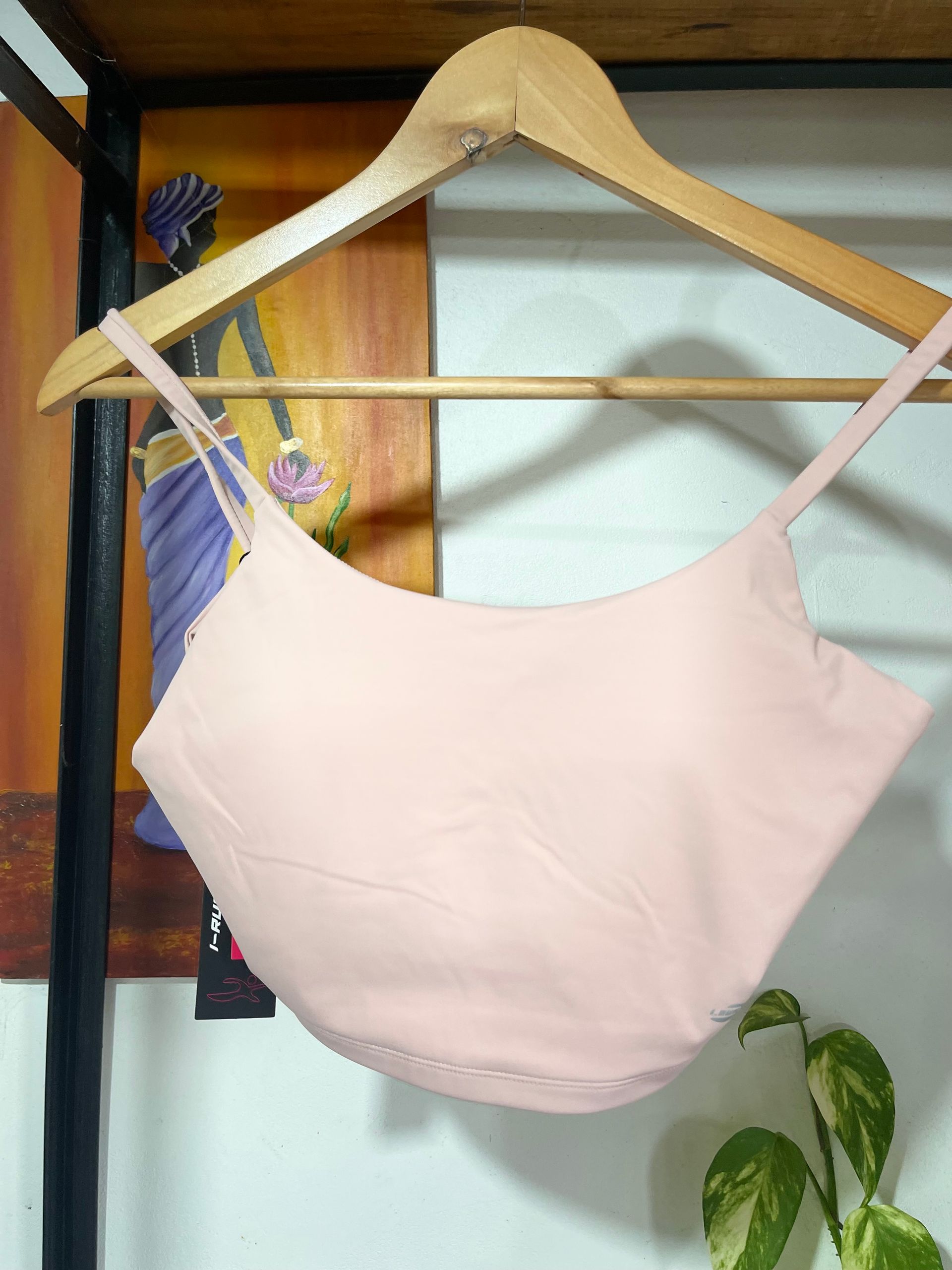 Un top corto rosa cuelga de una percha de madera.