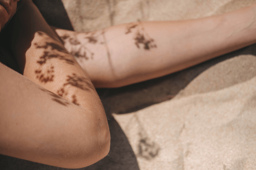 Person liegt im Sand, Blütenschatten zeichnen sich auf ihren Armen ab.