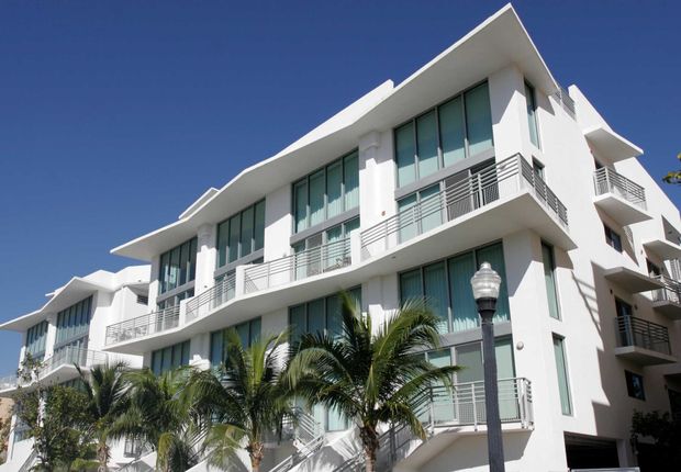 White apartment building with large windows and balconies, under a blue sky, palm trees in front.