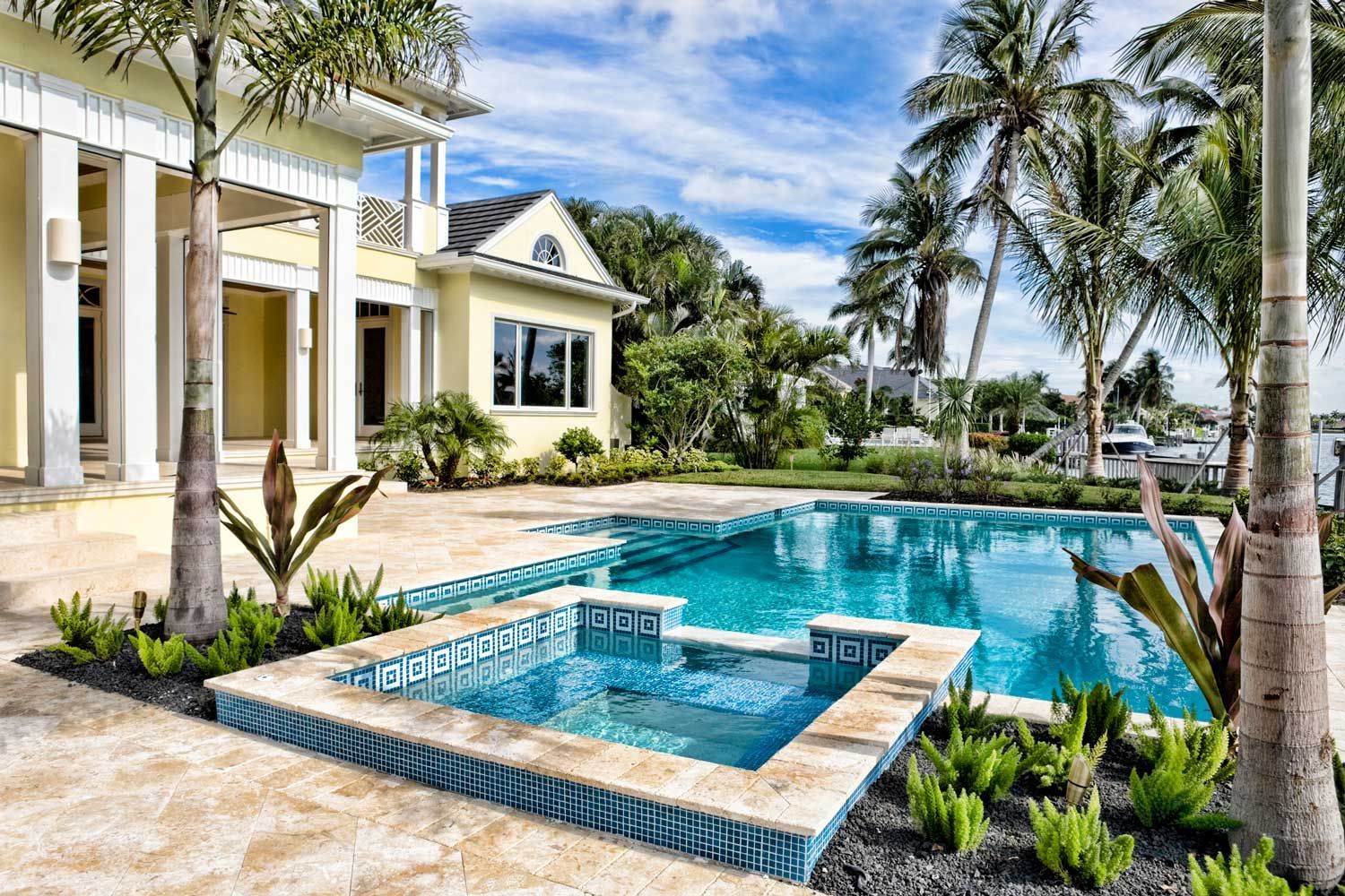 Luxury home with pool and spa, palm trees, blue water, sunny day.