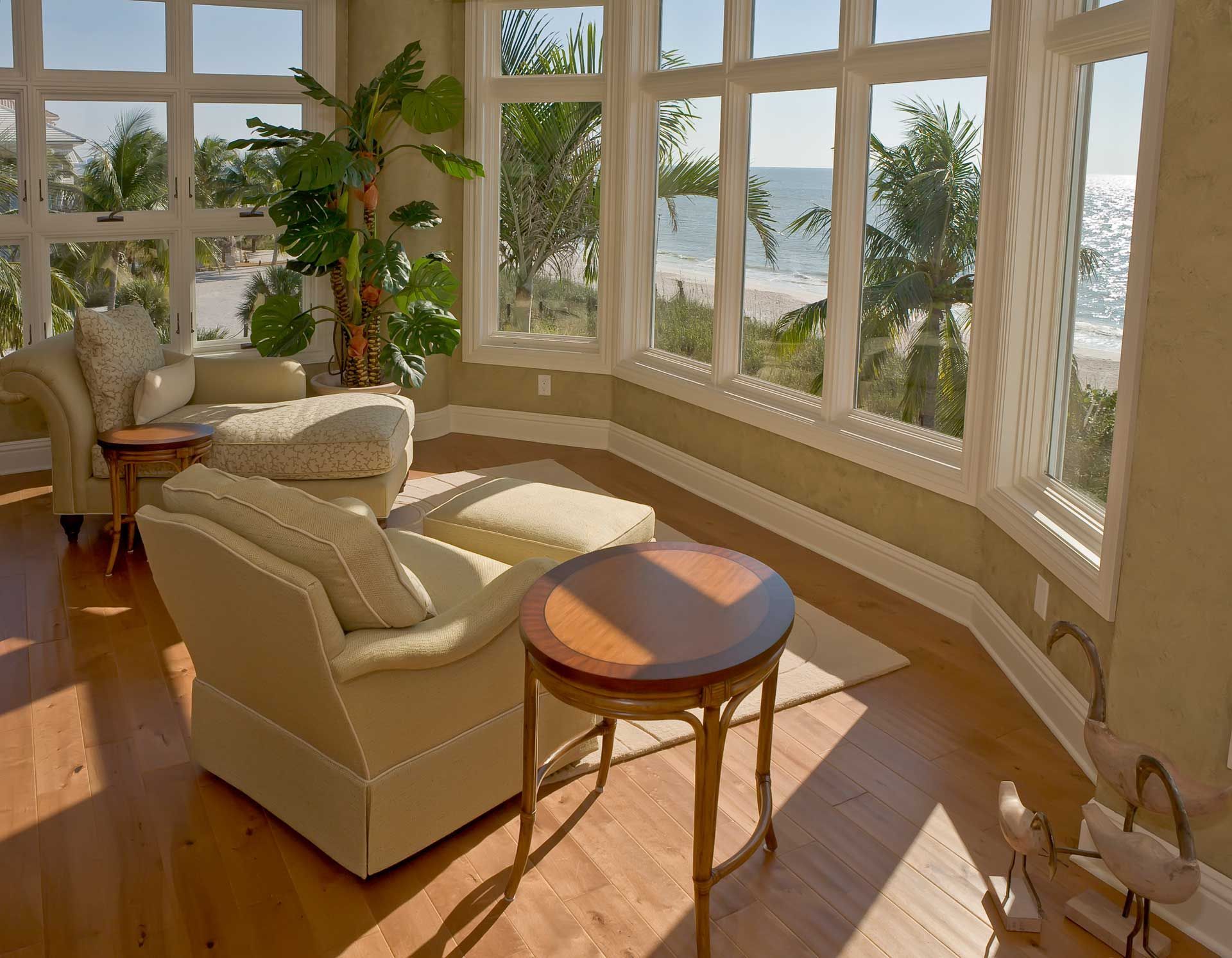 Bright sunroom with beach view, beige seating, wood floors, and round table.