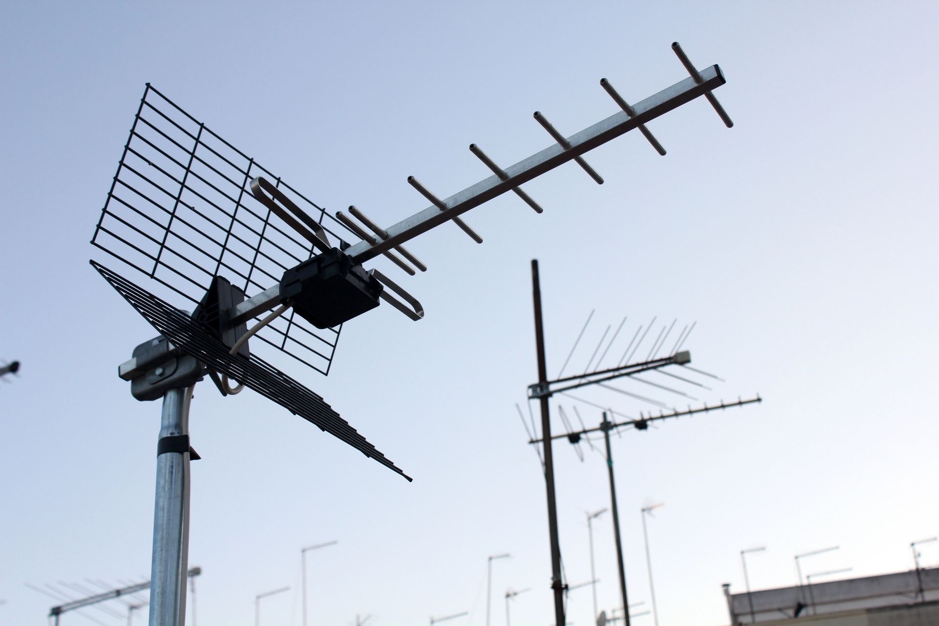 Antenne televisive sui tetti stagliano un cielo pallido, una grande antenna nera in primo piano.