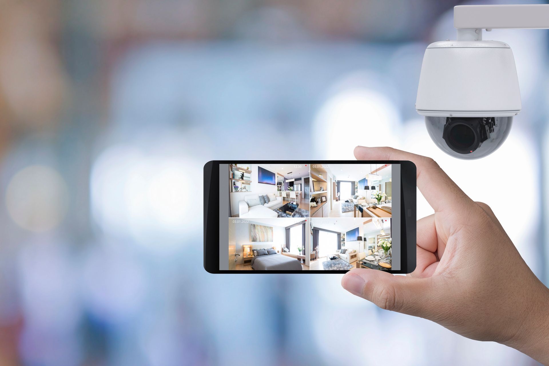 Una mano che tiene uno smartphone mostrando le immagini di una telecamera di sicurezza domestica, accanto a una telecamera di sorveglianza a cupola bianca.