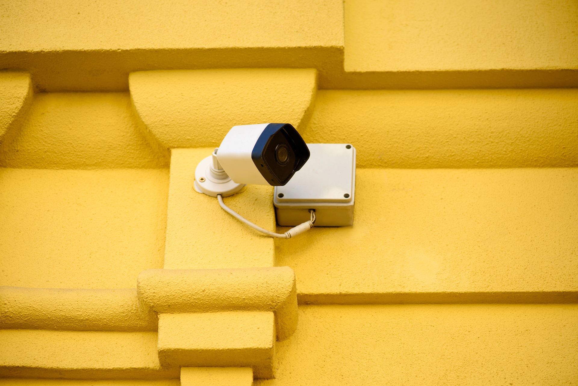 Telecamera di sicurezza bianca montata su una parete gialla, rivolta verso l'esterno.