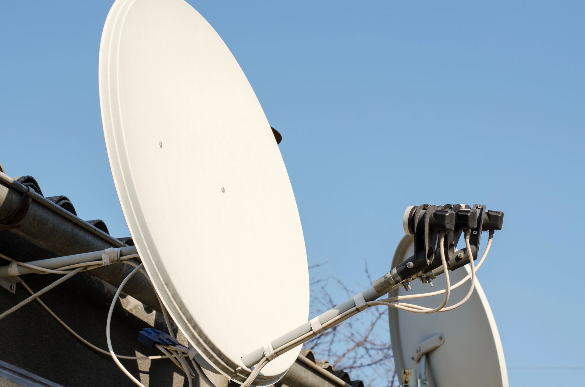 Due parabole satellitari bianche contro un cielo azzurro, con cavi e apparecchiature montate.