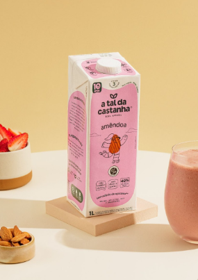 Caixa de leite de amêndoa rosa com smoothie de morango e ingredientes sobre uma superfície branca.