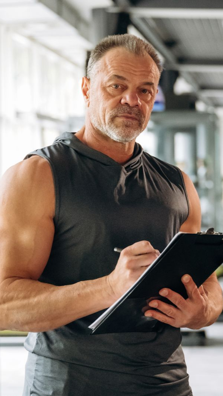 Homem de camisa preta falando ao microfone, segurando um controle remoto, com um cenário de palco ao fundo.