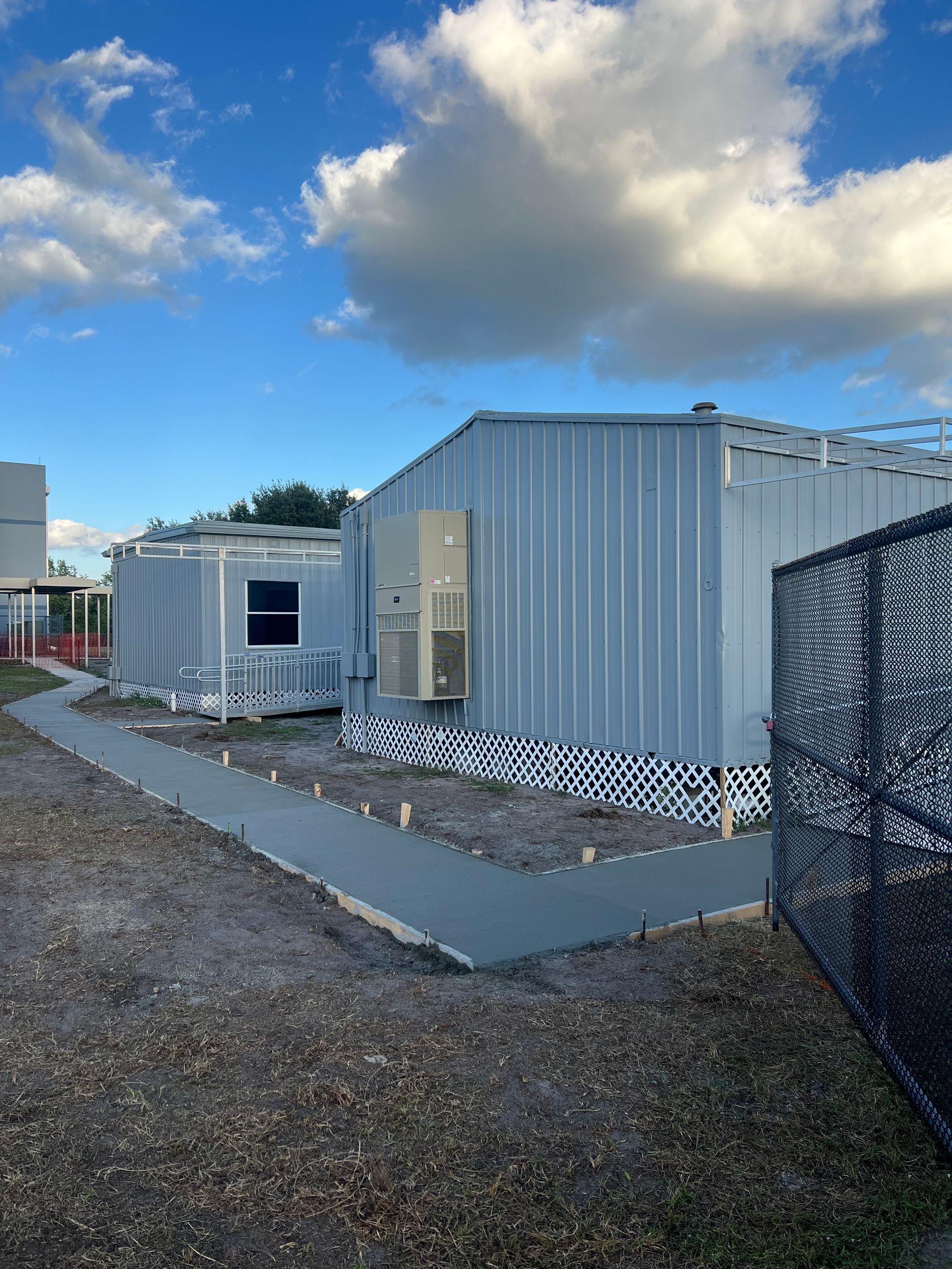 Exterior view of modular buildings with a concrete path, a blue sky, and a chain-link fence.
