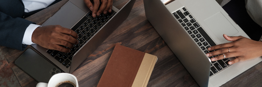 A man and a woman are sitting at a table using laptops.