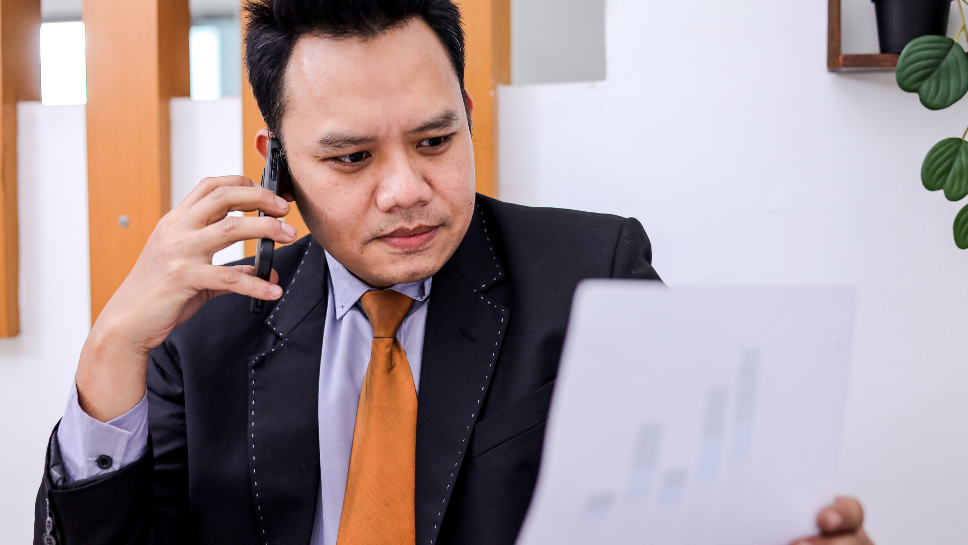 Man in suit on phone, looking at a document with a rising bar graph.