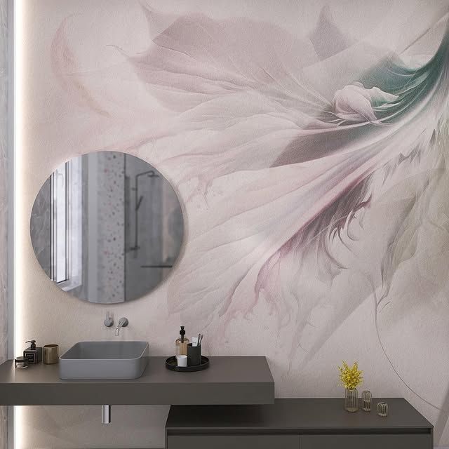 Un bagno con un murale a parete raffigurante petali astratti rosa e verdi, uno specchio rotondo e un mobile lavabo sospeso grigio.