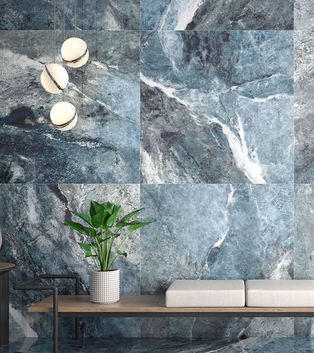 Una parete rivestita di piastrelle con motivo effetto marmo blu, una piccola pianta in vaso, una panca in legno con cuscini bianchi e moderne lampade a sospensione a forma di globo.