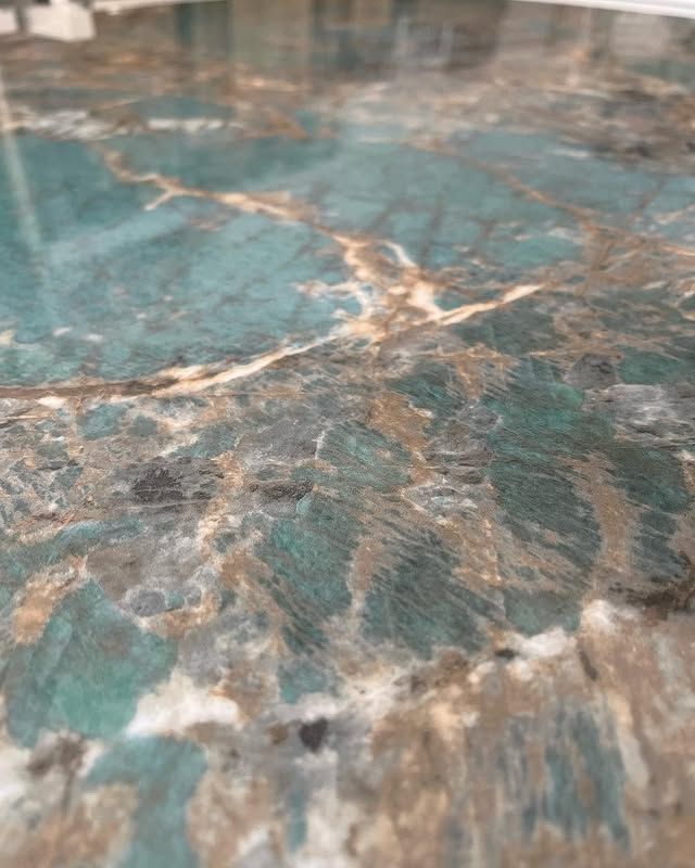 Vista ravvicinata di una superficie di marmo lucidato, nei toni del verde acqua e del marrone, con venature minerali naturali di colore chiaro.