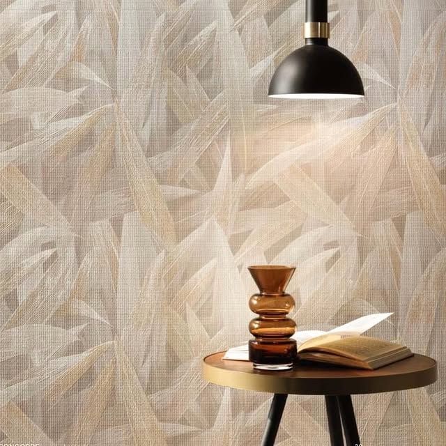 Sopra un tavolino rotondo, su cui poggiano un vaso di vetro marrone e un libro aperto, si staglia una moderna lampada a sospensione, sullo sfondo di una carta da parati astratta.